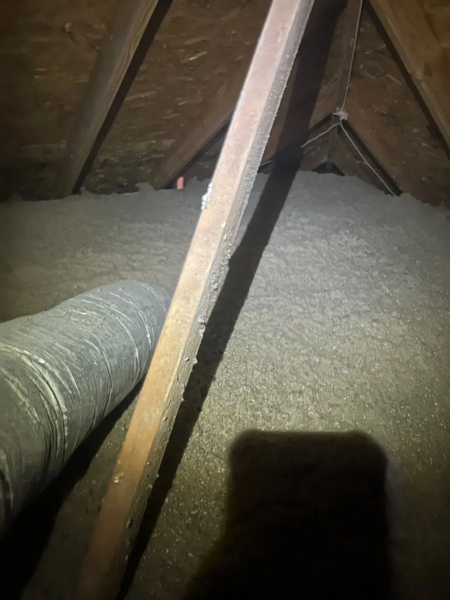 Cellulose insulation installed around attic framing with a flexible duct along the floor