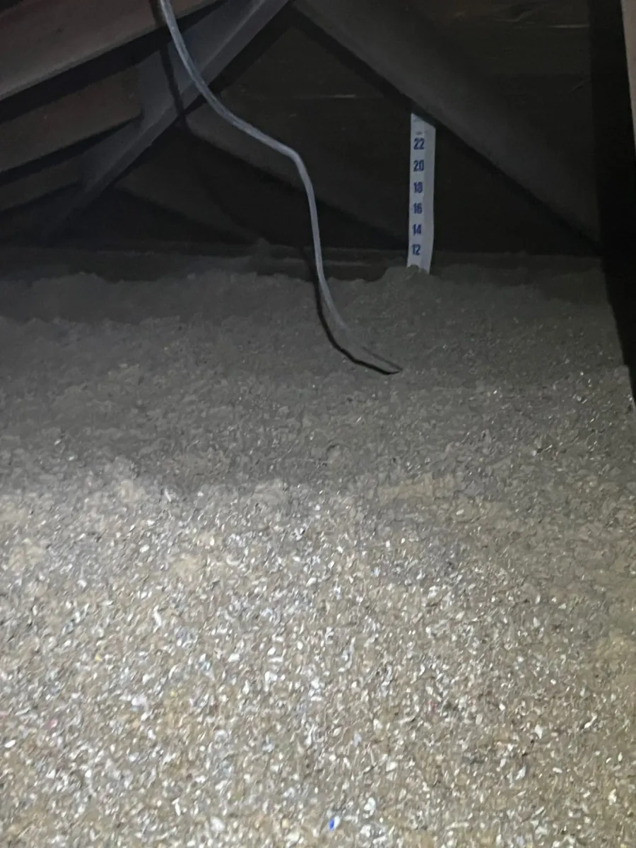 Cellulose insulation beneath a sloped attic roof with a measuring ruler and electrical cable visible
