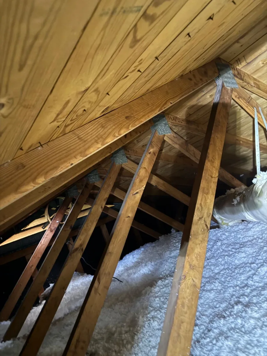 White fiberglass insulation spread across an attic floor under wood rafters